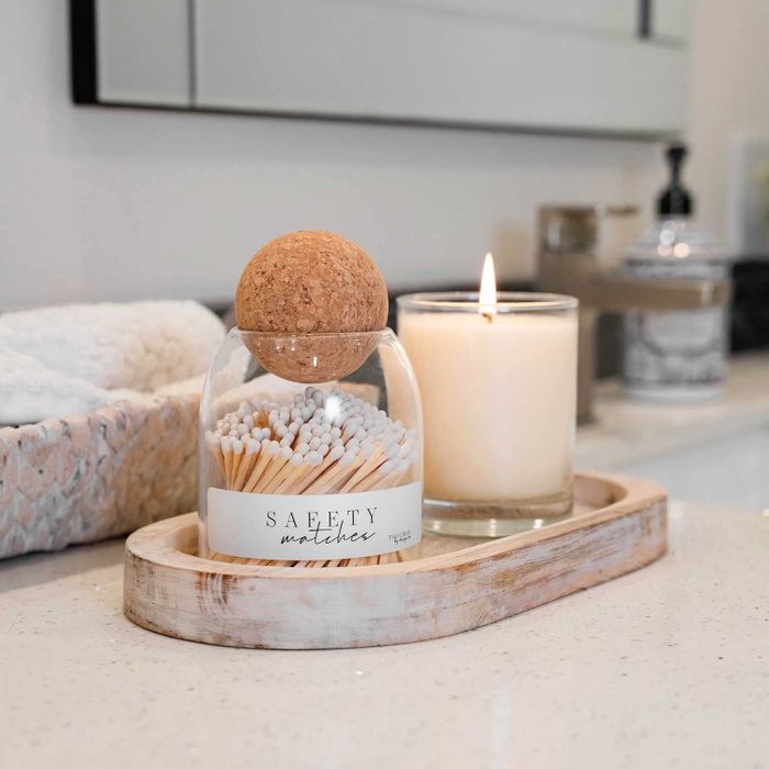 A sleek glass jar filled with neatly arranged matches, sealed with a cork ball on top.