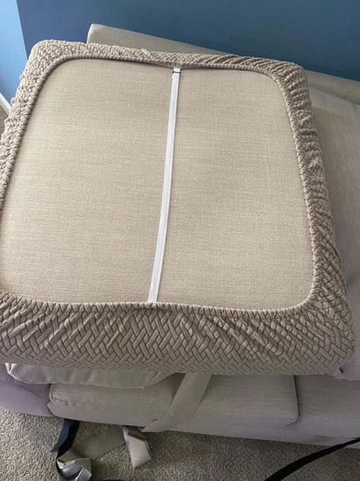 A beige square cushion with a zippered cover placed on a beige armchair, emphasizing the texture and design of the cushion.