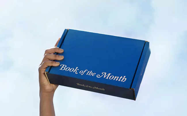 a hand holds a blue cardboard box labeled 'Book of the Month'