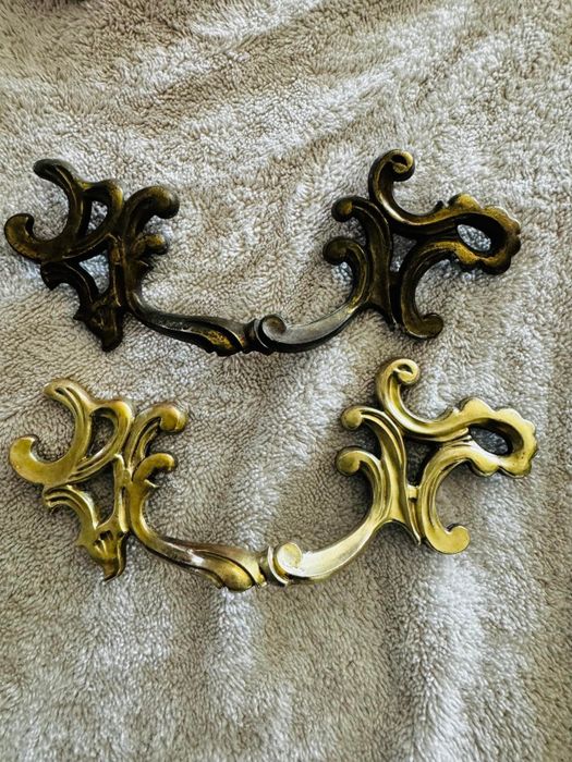 Two sets of intricately designed, vintage-style drawer pulls placed on a textured surface.