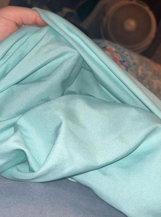 A hand holding soft, folded fabric, displayed indoors near a fan