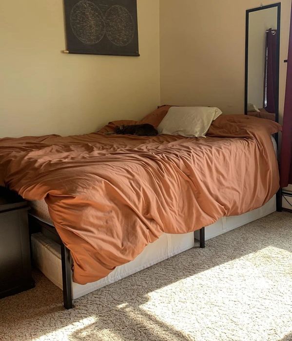 A neat bedroom featuring an unmade bed with a duvet, artwork hanging above, and a full-length mirror