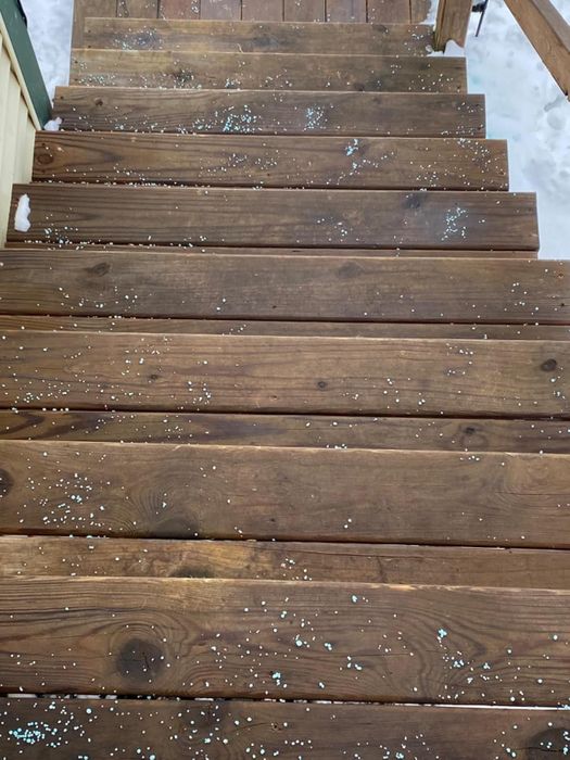 Wooden steps covered with de-icing pellets, leading toward a snow-covered area