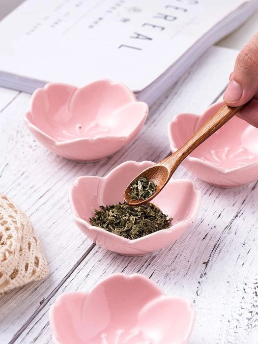 A model using a spoon to scoop herbs from a pink cherry blossom dish