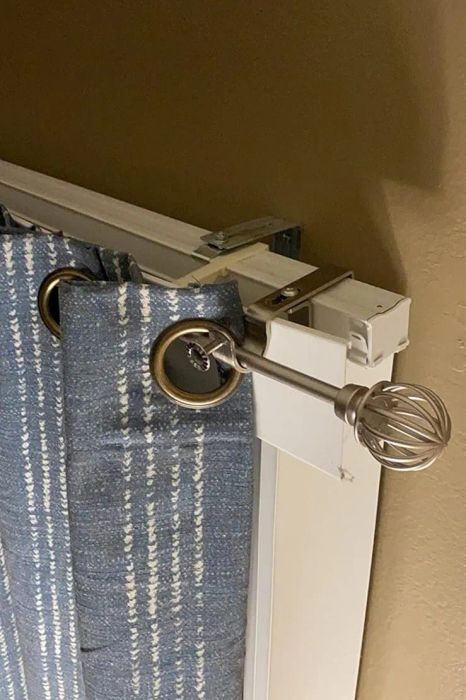 A curtain rod with an ornate finial and blue striped curtains hanging from a wall