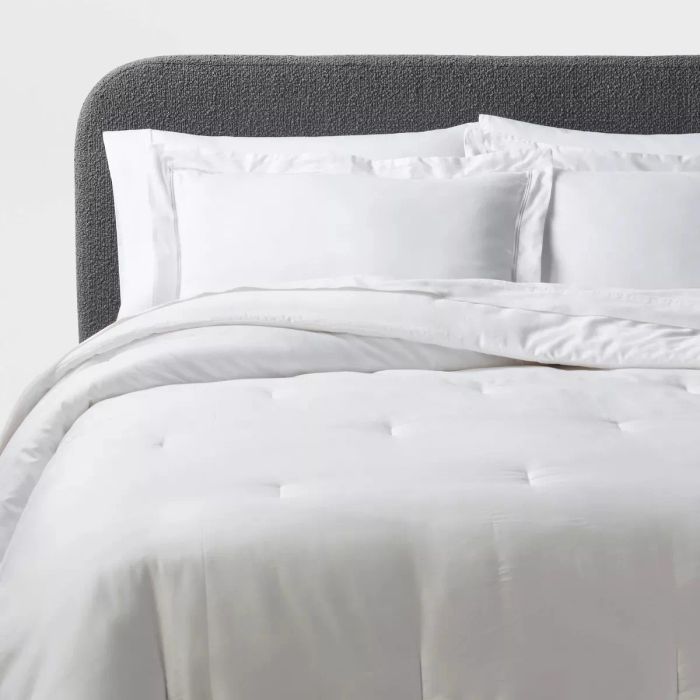 A bed with a collection of pristine white pillows, a cozy comforter, and an elegant tufted headboard.
