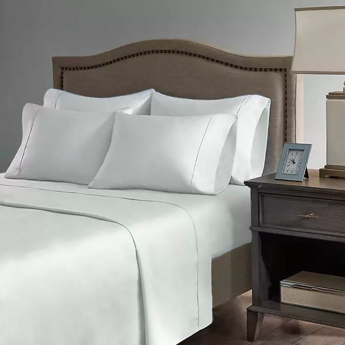 A bedroom featuring a neatly made bed with white sheets and pillows, next to a nightstand adorned with a lamp and a framed picture