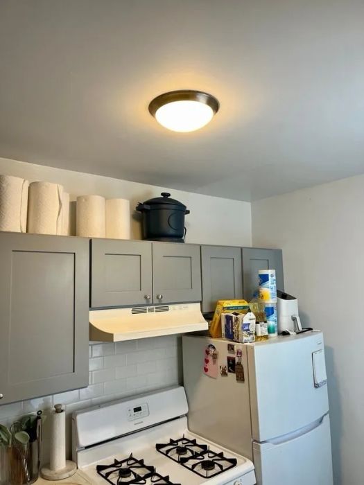 A kitchen with a stovetop, cabinets, and a refrigerator, with various kitchen essentials placed above the cabinets and on top of the fridge.