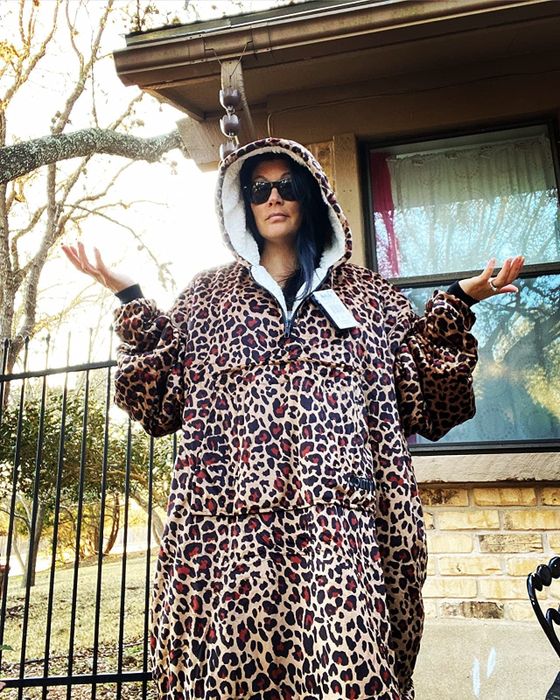 A reviewer steps outdoors wearing the leopard-print hoodie blanket, embracing comfort while braving the elements.