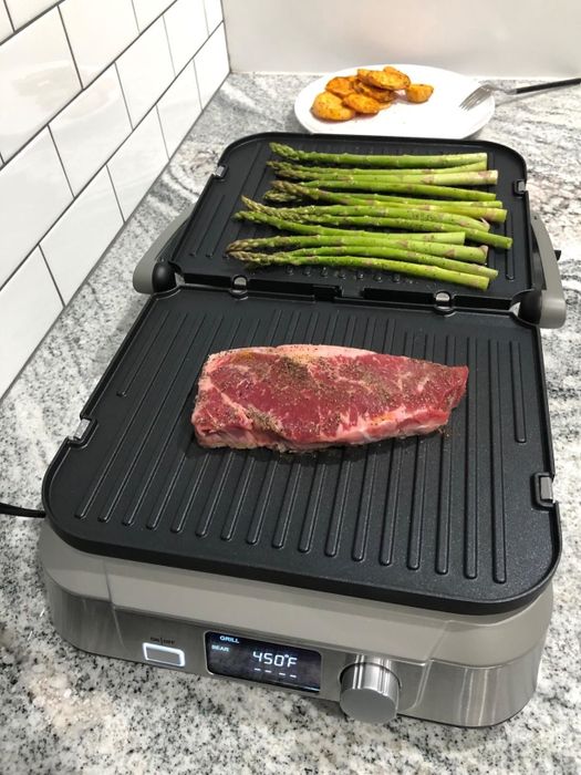 A reviewer's grill in action, featuring meat and asparagus sizzling on top.