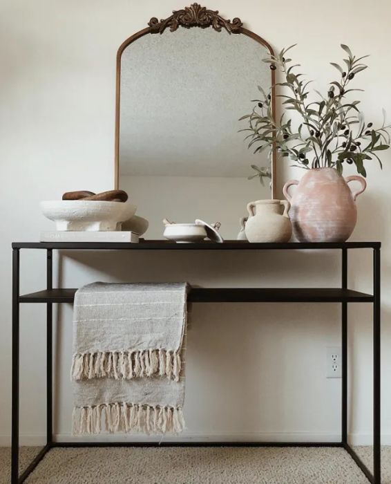 An arched mirror with intricate gilded detailing displayed on an entryway table.