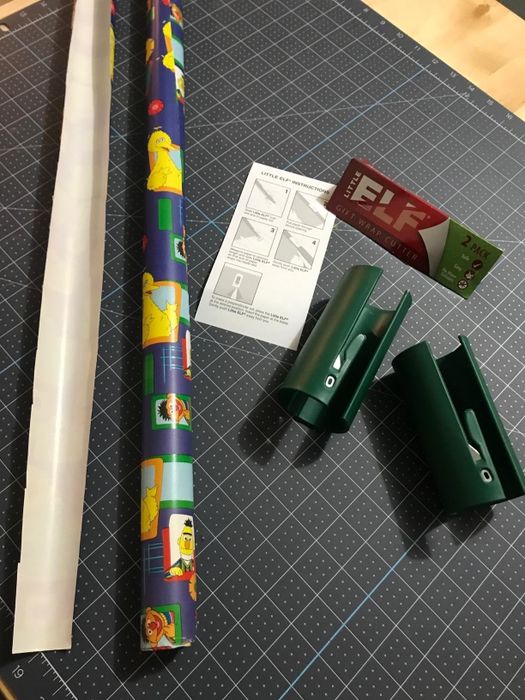 A roll of wrapping paper, instructions, and two green paper cutters placed on a cutting mat