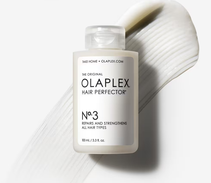 The bottle of Olaplex No. 3 Hair Perfector against a creamy backdrop of hair product streaks, designed to repair and strengthen all hair types.