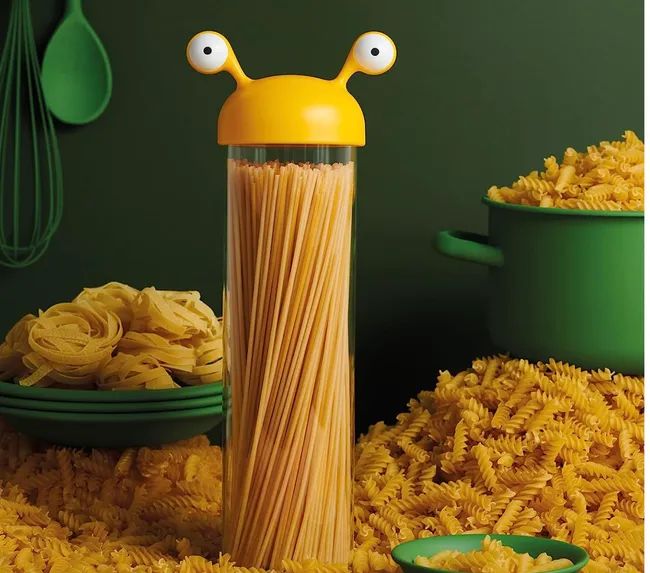 A clear, cylindrical container with a green monster-shaped lid, filled with noodles