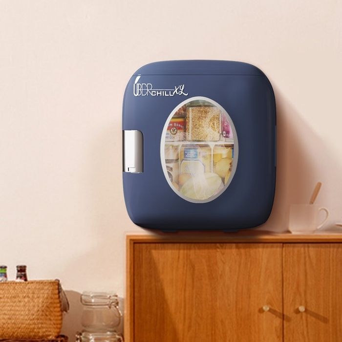 A small mini fridge stocked with drinks and snacks, placed on a wooden cabinet in a charming kitchen setup