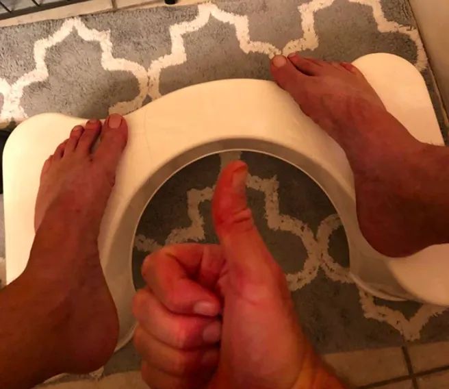 A customer review photo showing their feet resting on the Squatty Potty around the toilet, with a thumbs up gesture