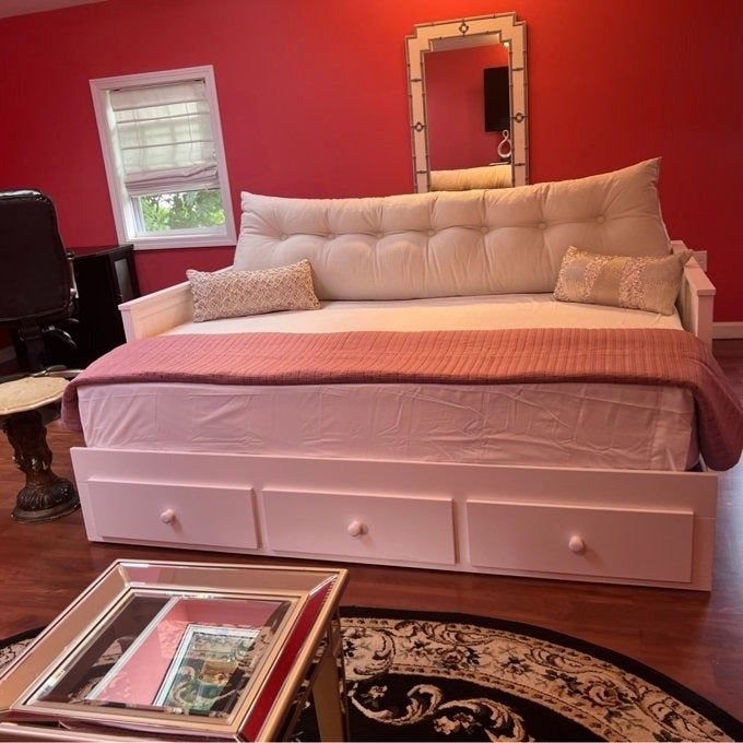 A stylish home office featuring a daybed with a white cushioned backrest, decorative throw pillows, and practical drawer storage