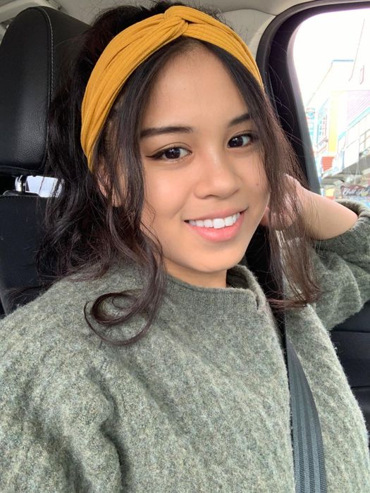 Person smiling inside a car while wearing a casual knit sweater and headband