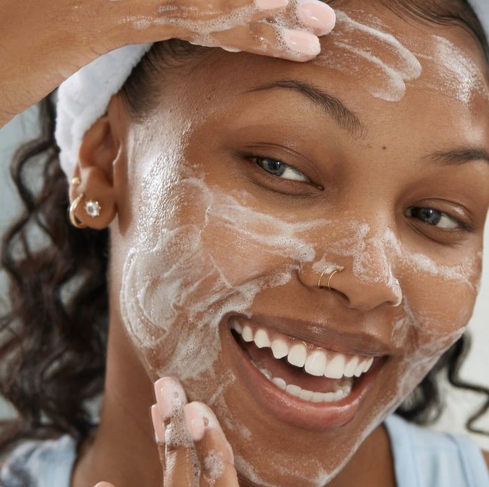A model smiling while applying foamy face wash.