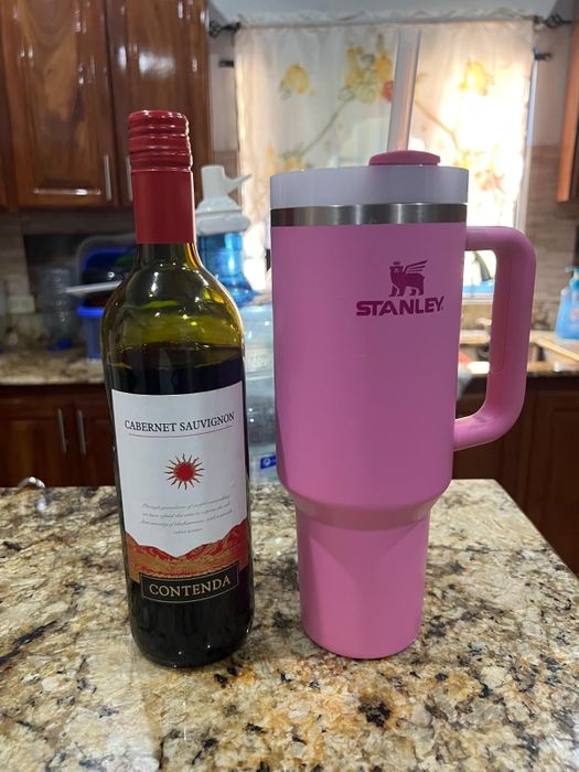 A bottle of Contenda Cabernet Sauvignon paired with a large pink Stanley tumbler with a straw on a kitchen counter.