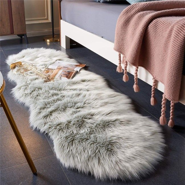 A faux-fur rug laid out next to a bed.