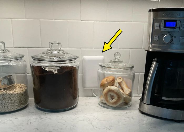 Kitchen countertop with three glass jars holding oatmeal, coffee, and bagels, next to a shiny silver coffee maker