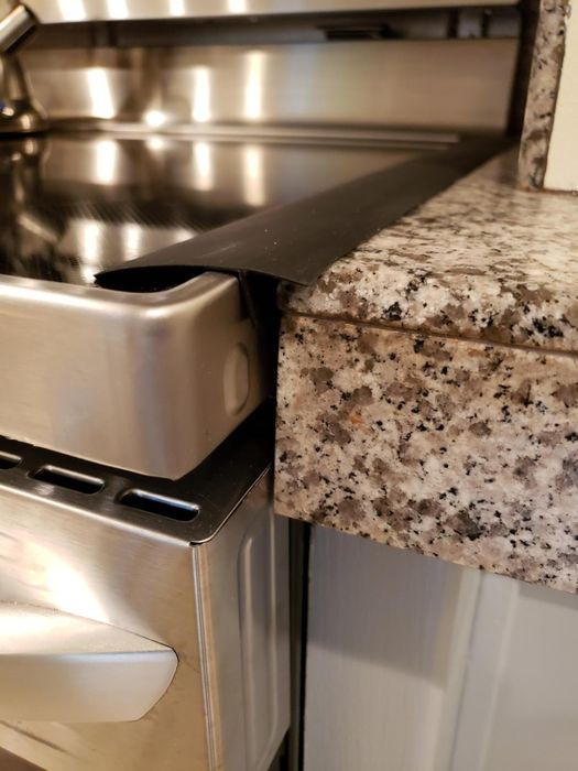reviewer showing a close-up of a stove gap cover bridging the space between counter and stove to prevent spills and make kitchen cleaning easier