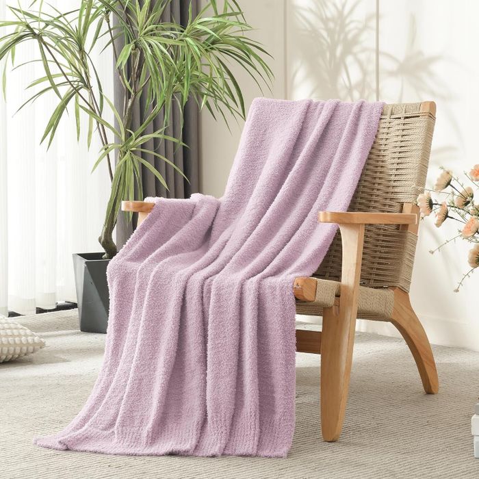 A comfy armchair with a plush throw draped over it, bathed in sunlight in a cozy living room filled with greenery.