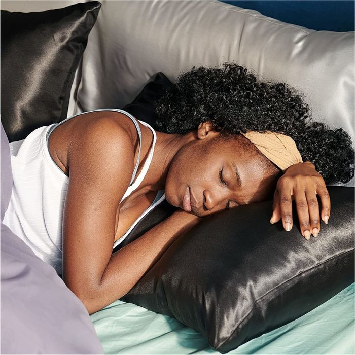 A model relaxes on a pillow with a luxurious black satin pillowcase.