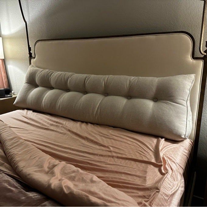 A plush headboard pillow resting on a neatly made bed, showcasing a cozy and inviting bedroom shopping option