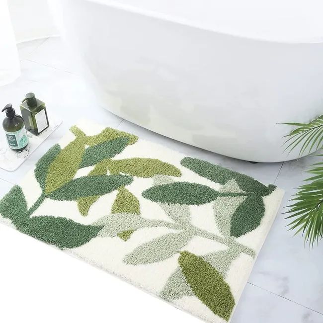 A white bath mat featuring leaves in three shades of green placed in front of a bathtub.