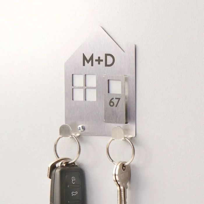 A house-shaped key holder with initials and a house number, featuring space for two key rings, mounted on a wall.