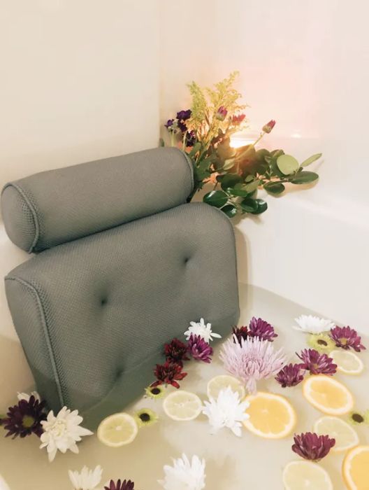 A reviewer's tranquil bath, filled with vibrant flowers and slices of citrus, complete with a back and neck pillow attached to the bathtub