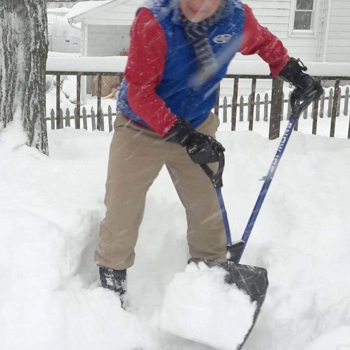 A person shoveling snow in their yard, dressed warmly in gloves, a scarf, and boots