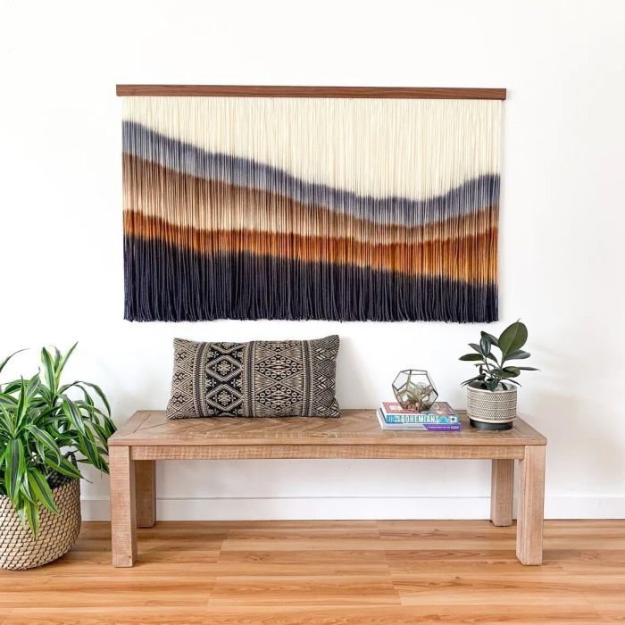 A large macrame piece in gray, orange, and gray, hanging elegantly above a bench.