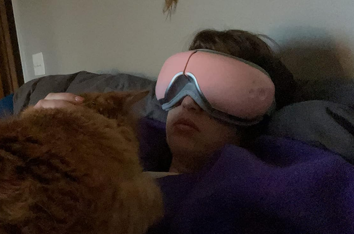 A person unwinding with a sleep mask, cuddling a cat on the bed, suggesting comfort and relaxation.