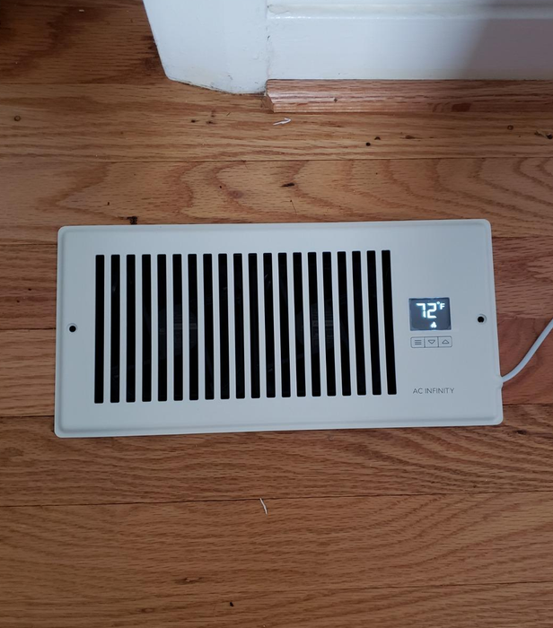 A reviewer’s photo showing the booster fan installed on a floor vent