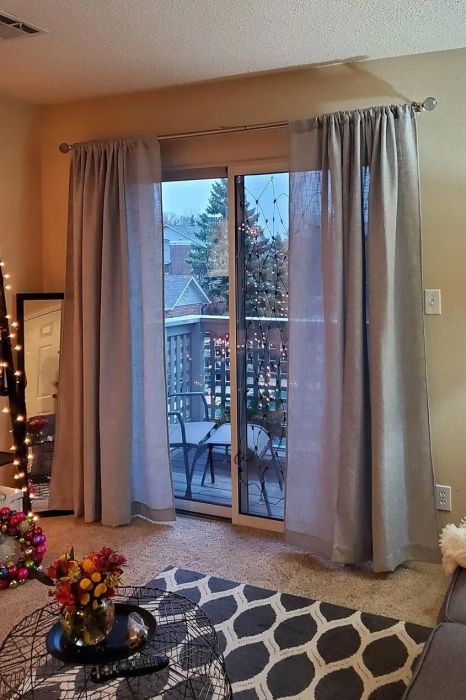 A cozy living room with sheer curtains, a balcony view, string lights, and a well-decorated shelf, creating an inviting space perfect for unwinding