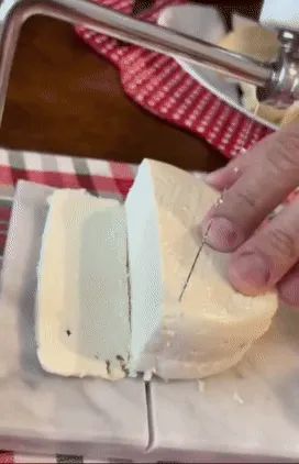 A reviewer uses the white marble cheese slicer to neatly cut through soft cheese with its wire