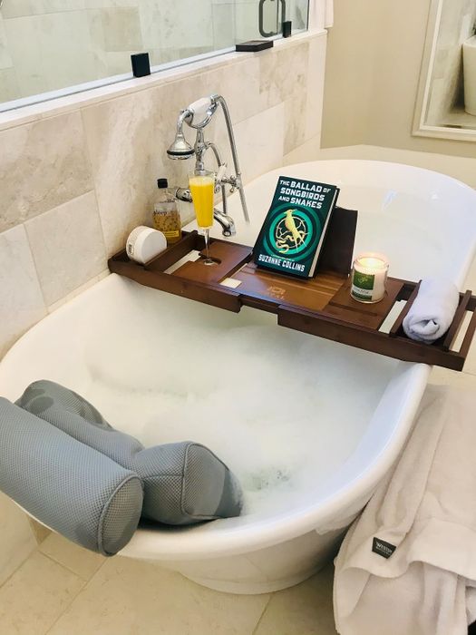 A lavish bathtub setup complete with a book, candle, towel, drink, and bath essentials neatly arranged on a wooden tray. Perfect for an indulgent at-home spa retreat.