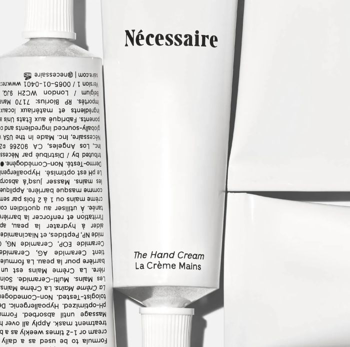 A tube of Nécessaire Hand Cream with minimalist packaging, positioned with its boxes