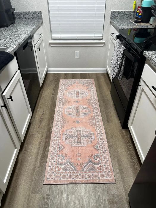 A tidy kitchen featuring white cabinets, sleek granite countertops, and a stylish patterned runner rug on the floor, surrounded by various kitchen essentials.
