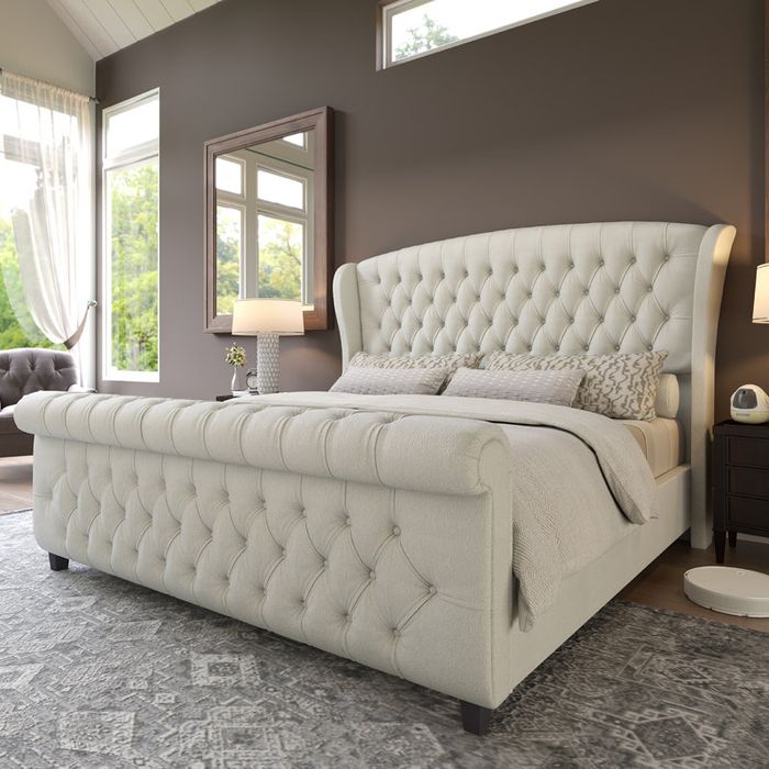 A luxurious tufted bed in a sunlit room, adorned with decorative pillows and a patterned rug, creating a cozy and refined ambiance for a shopping feature