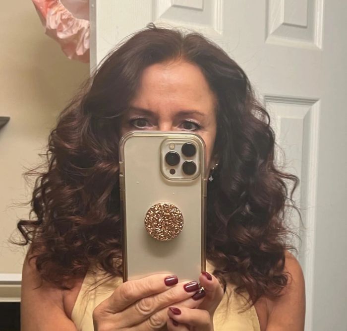 A person with curly hair snapping a mirror selfie