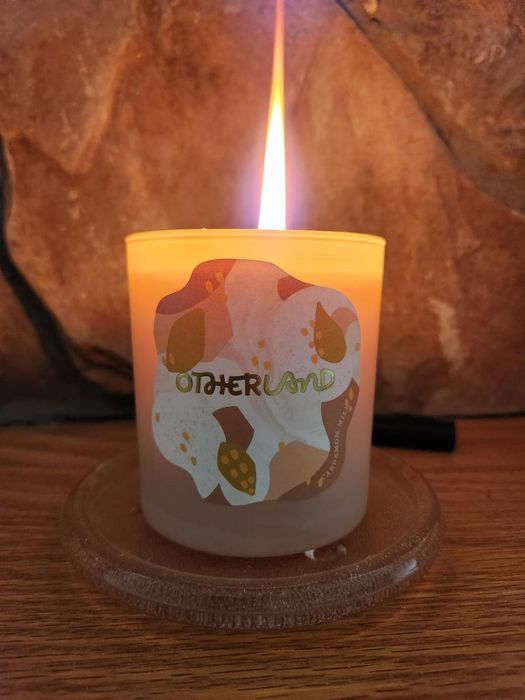 A lit Otherland candle with its label clearly visible.