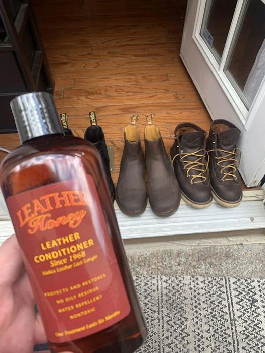 reviewer showcasing the leather conditioner bottle in front of multiple pairs of leather boots