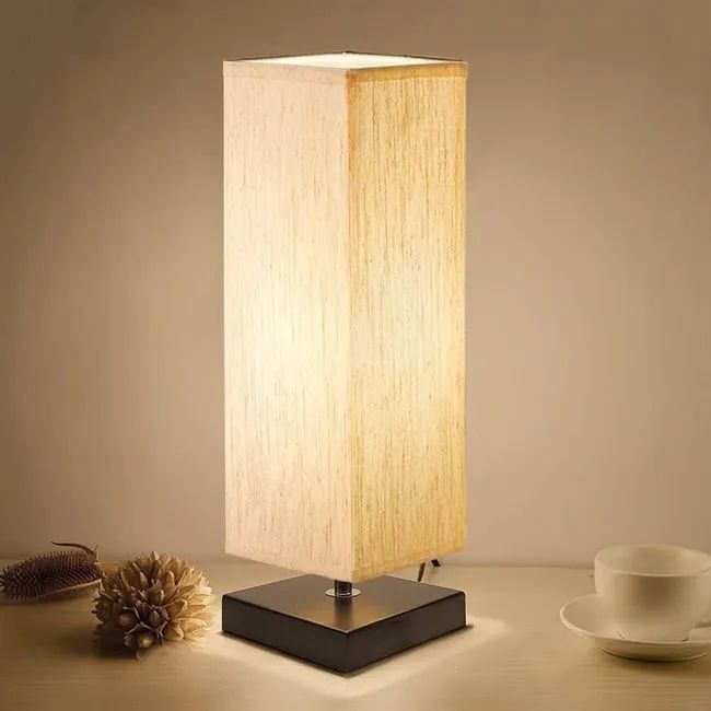 A lamp with a square fabric shade in a tan color, paired with a dark brown wood base.