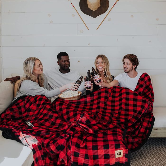 Four individuals comfortably nestled inside a gigantic black and red checkered blanket.