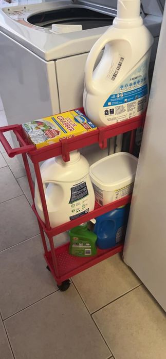 A rolling cart in a laundry room holding detergent, baking soda, and cleaning supplies next to a washing machine.