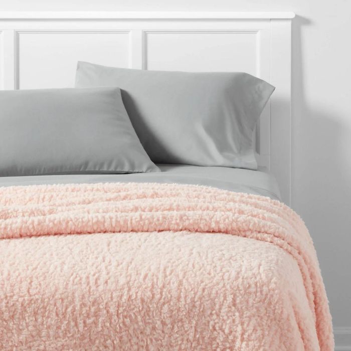 A bed featuring a white headboard, a gray pillow, and a plush pink blanket for that ultimate cozy look.